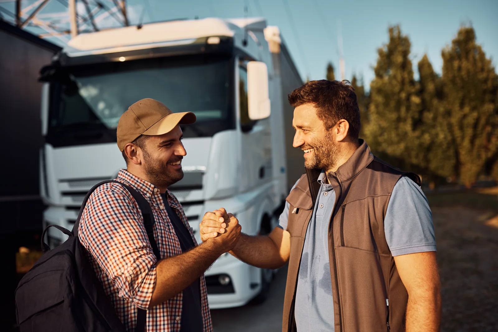Two truck drivers clasping hands in front of a white truck at sunset.