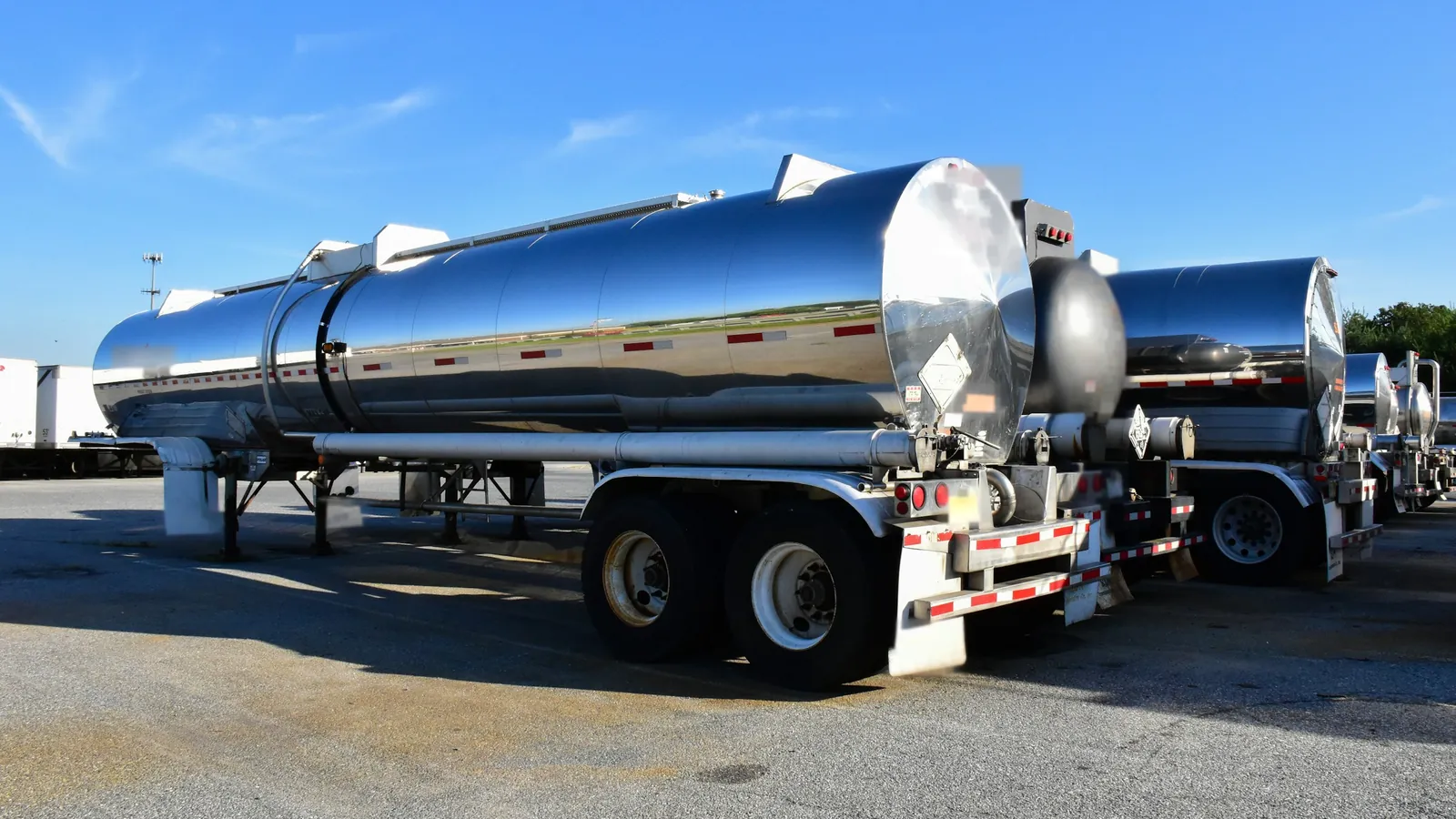 A row of polished stainless steel tanker trailers parked side by side in a lot.