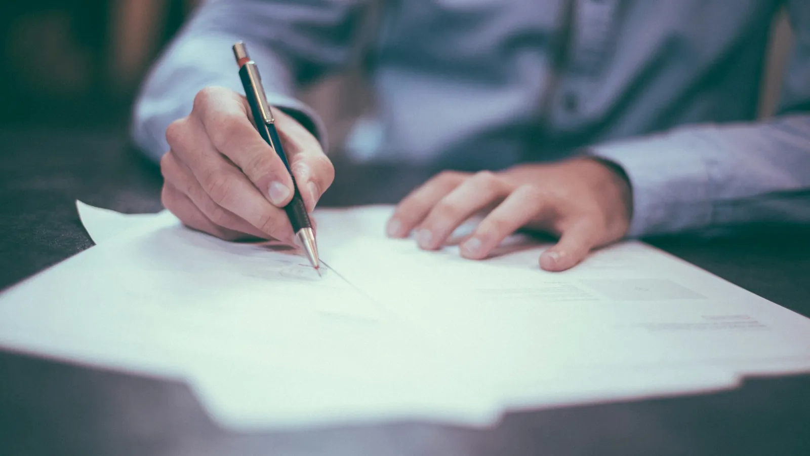 A person signing a printed document with a pen.