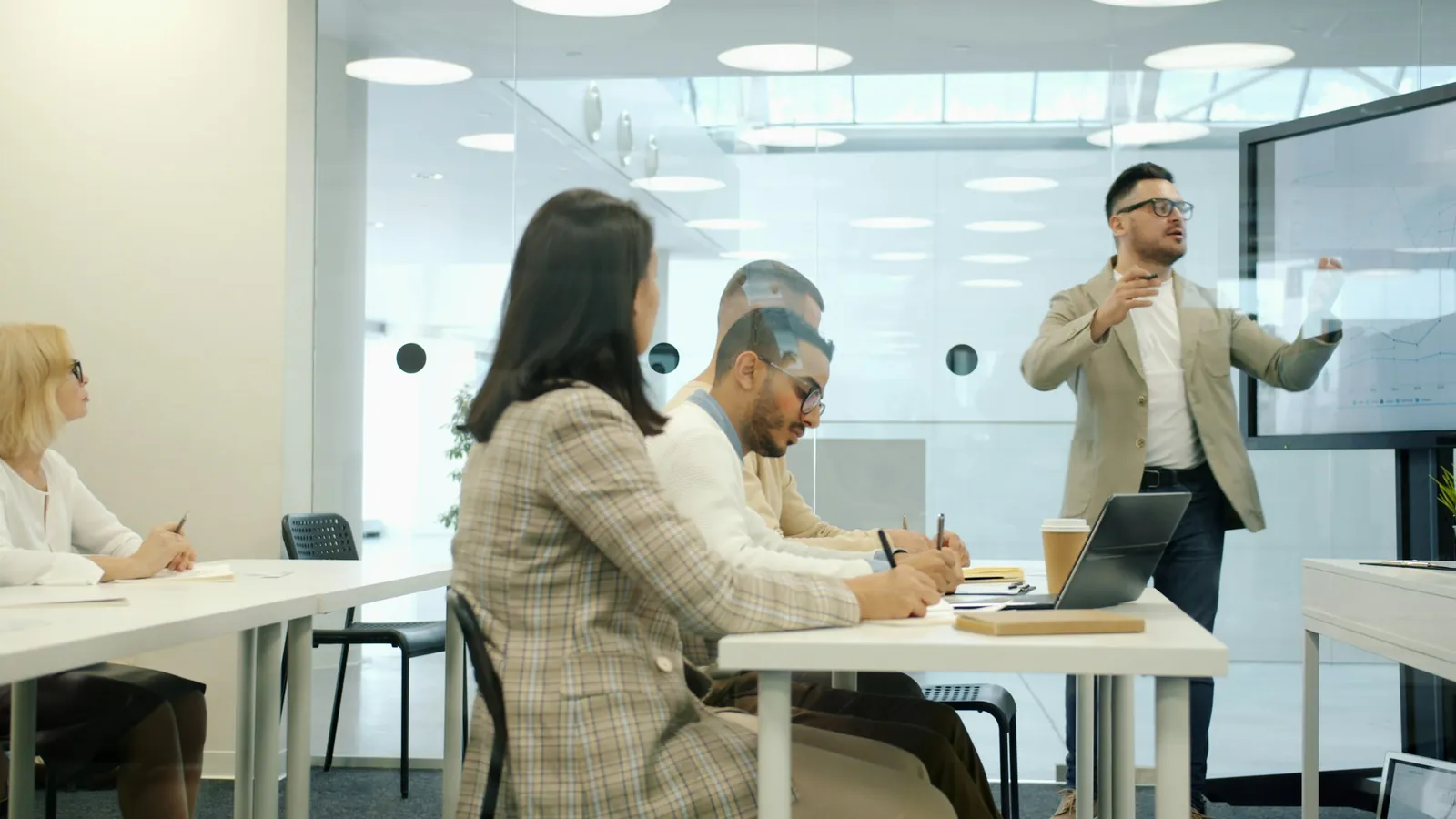 A presenter speaking to adults taking notes at a workplace training session.